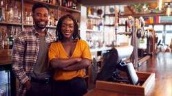 一对开酒吧的黑人夫妇站在柜台后面微笑着 